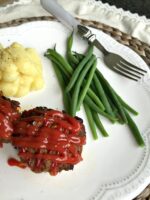 Meatloaf muffins with ketchup and green beans on a plate.