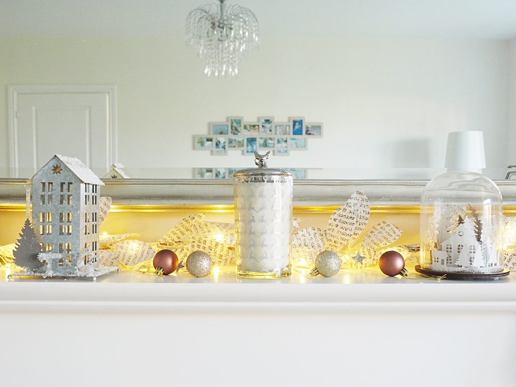 A mantlepiece lit up with fairy lights and decorated for Chirstmas