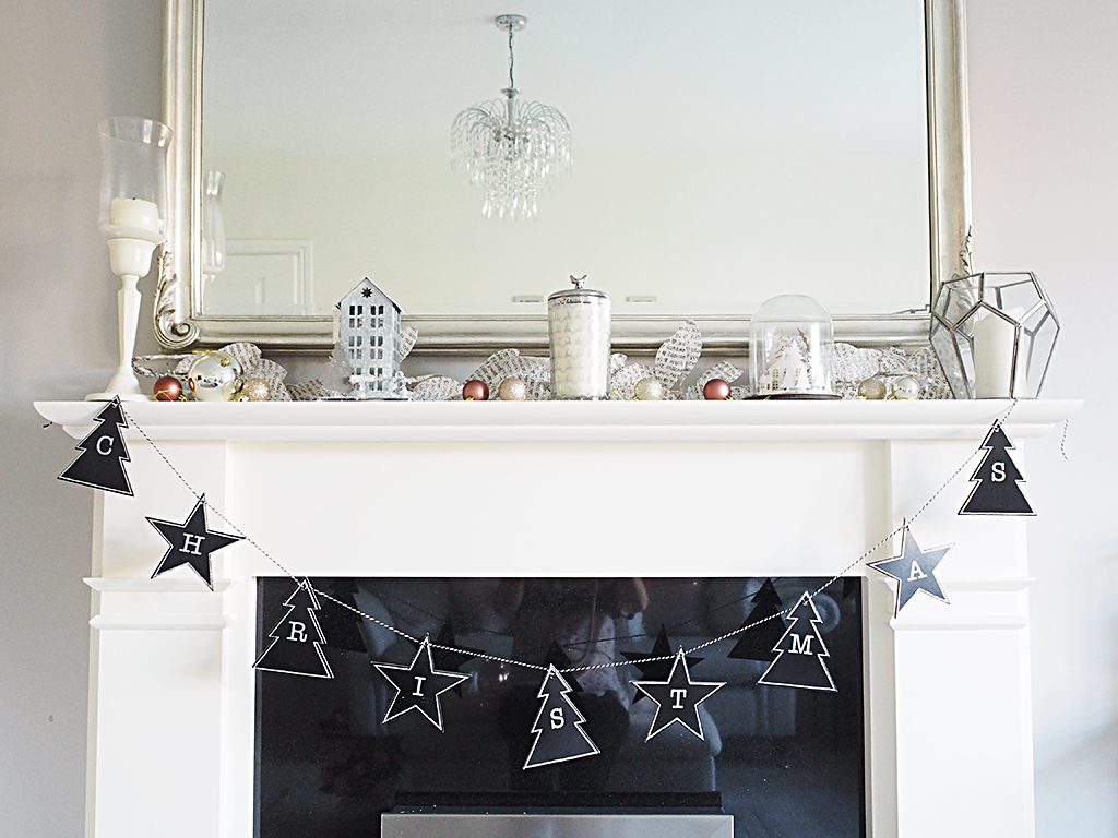 A fireplace mantle decorated for Christmas with candles, a black garland and silver and rose gold accent baubles