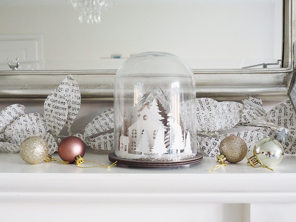 A Christmas snow globe surrounded by rose gold Christmas baubles