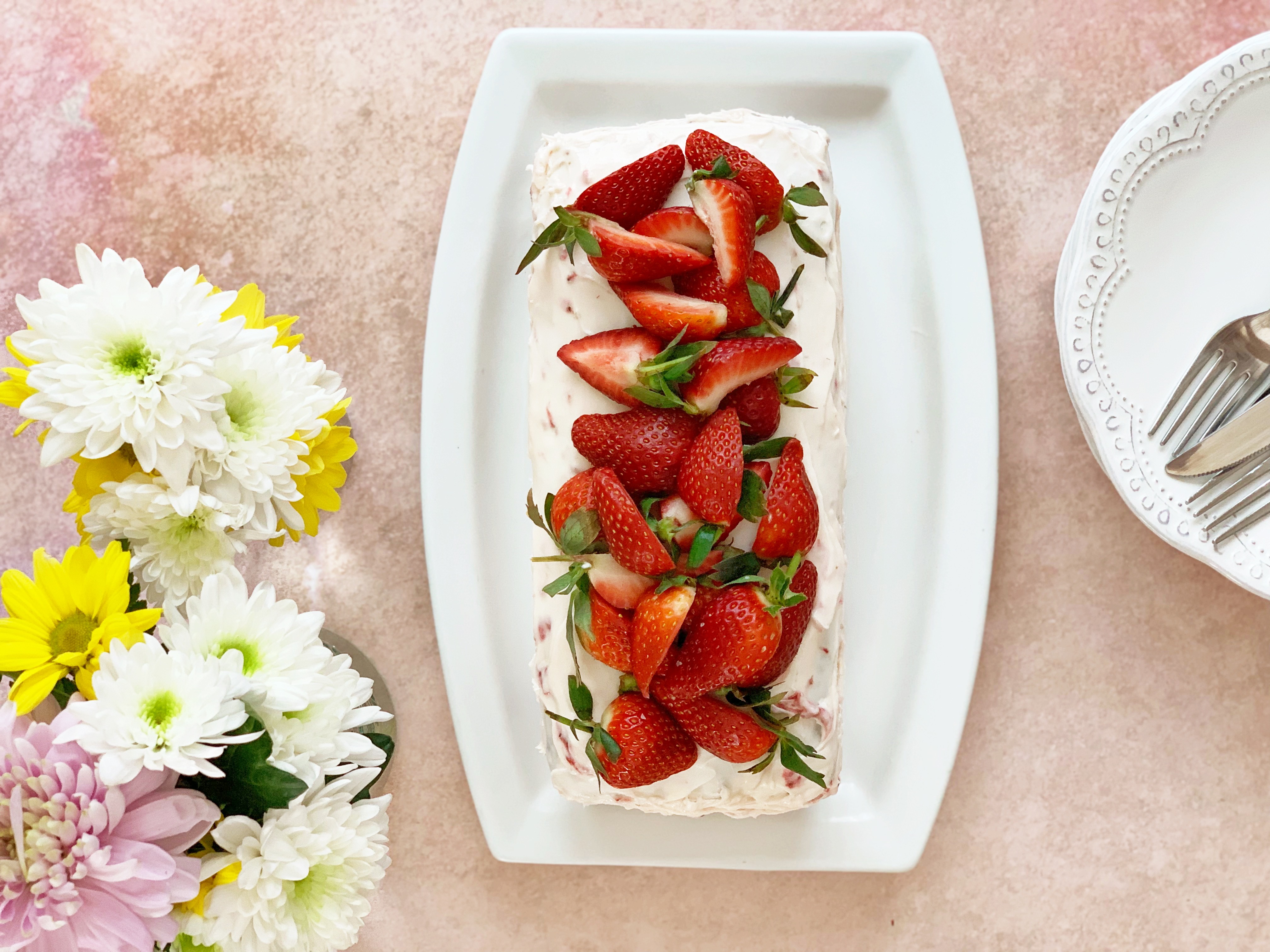 Strawberry bread with cream cheese frosting and fresh strawberries on top. To the left of it is a bunch of flowers in spring colours