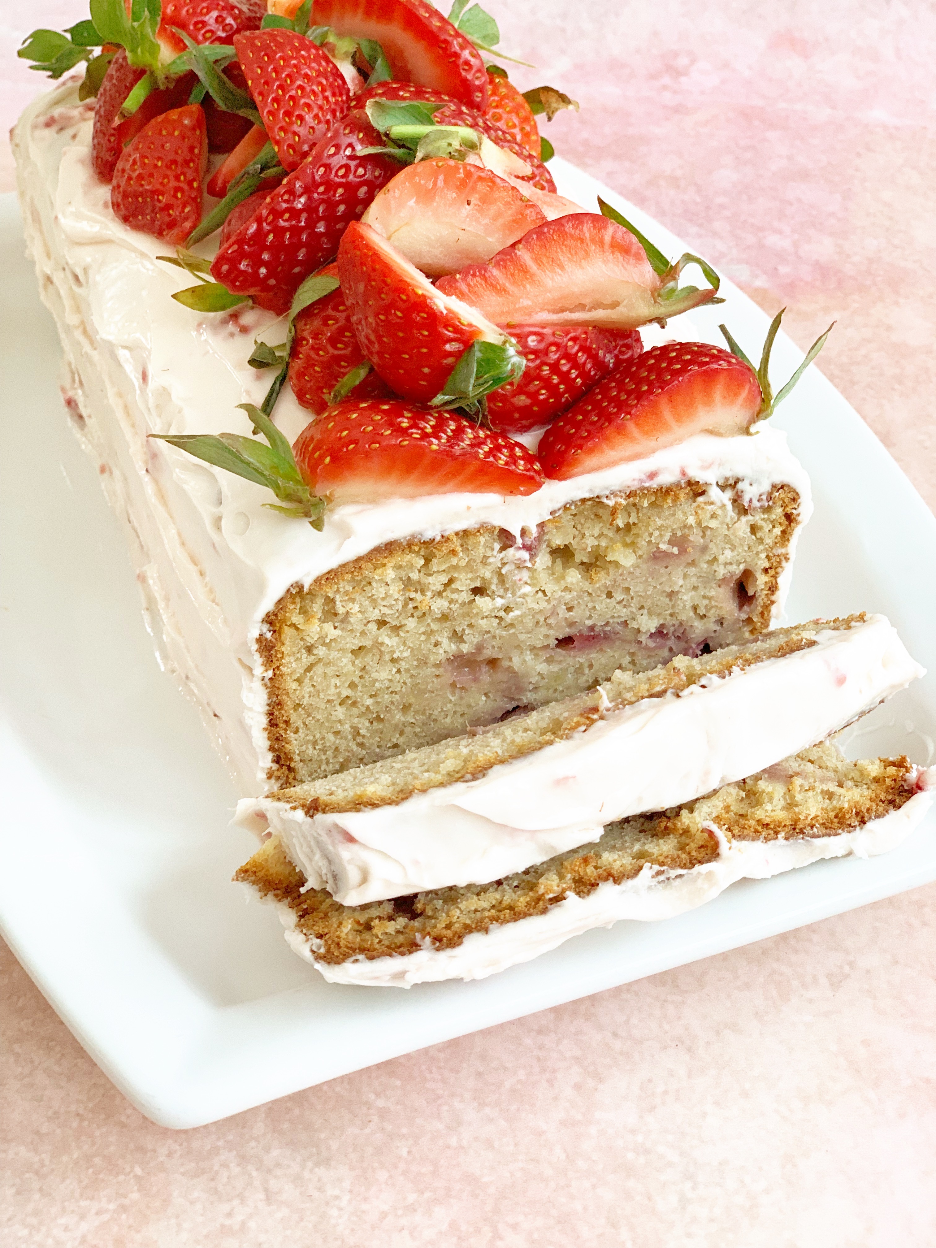 Strawberry bread with cream cheese frosting and fresh strawberries on top. 2 slices have been made in the end to show the internals of the bread