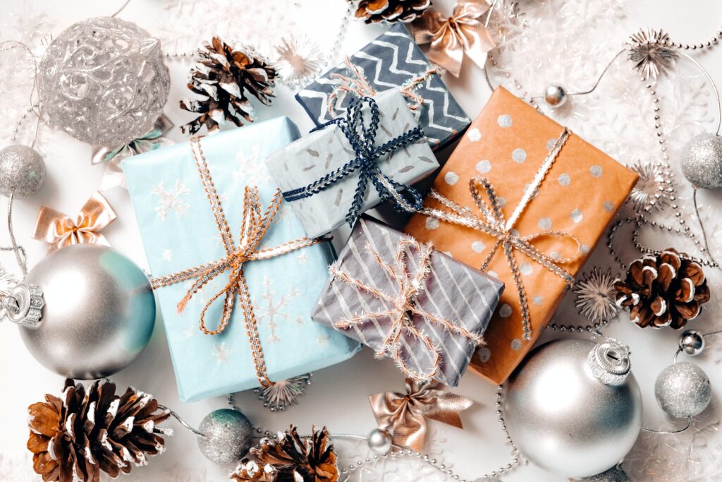 Beautifully wrapped Christmas presents with ribbons sit on a white background with frosted pinecones and silver baubles