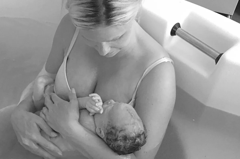 A black and white image of a woman in a birthing pool holding her new baby