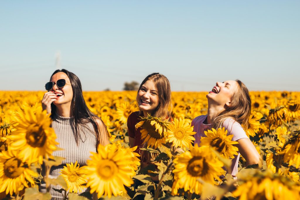 Three young women starting their day, laughing in a sunflower field.