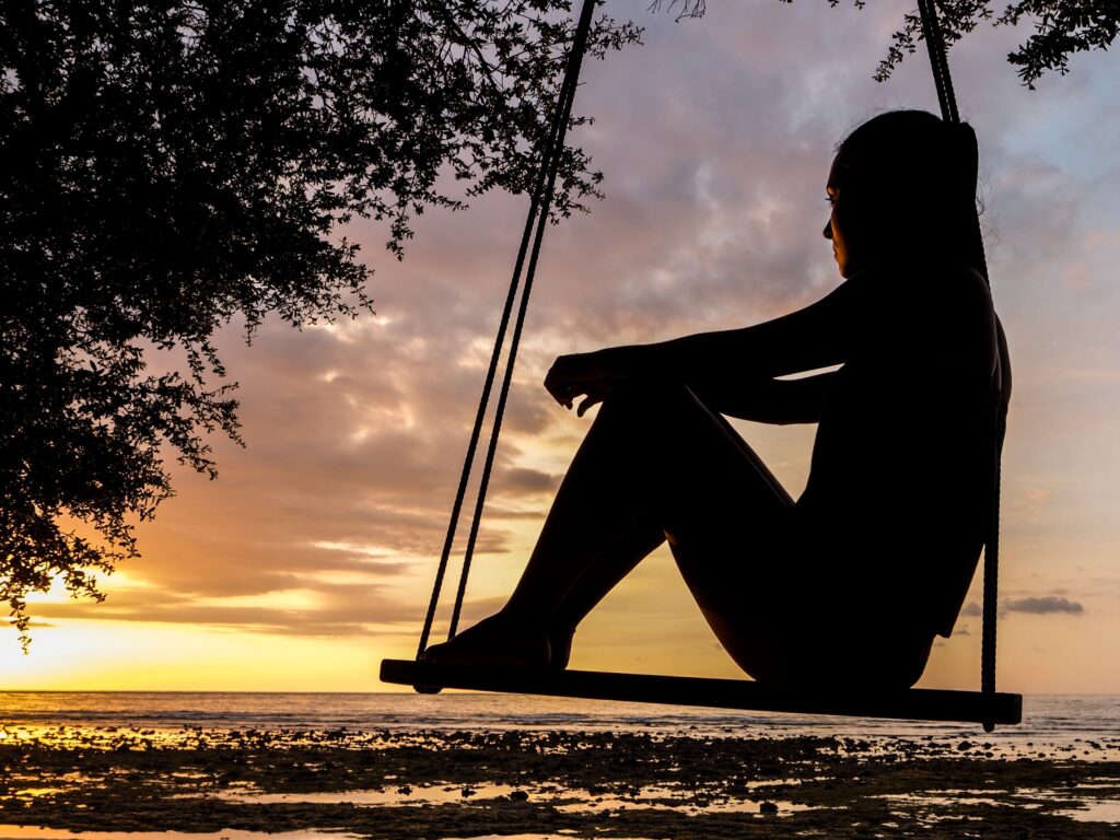 A silhouette of a woman on a swing at sunset, peacefully contemplating her hardest struggles.