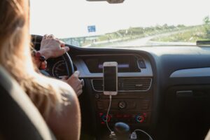 A woman, who is a driving instructor, is driving a car while holding a cell phone.