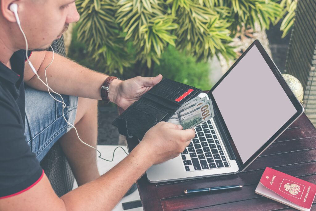 A man using a laptop with headphones and a passport, seeking financial boost.