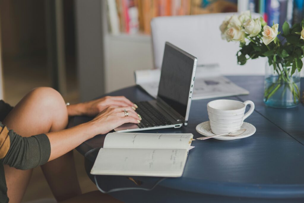 A woman, working as a pharmacy technician, sits at a table with a laptop and flowers, thus enjoying her rewarding career.