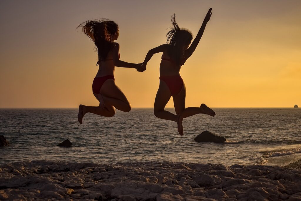 Two women jumping in the air on the beach at sunset, exemplifying a summer body.