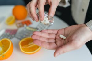 A woman is putting supplements into a jar next to oranges.