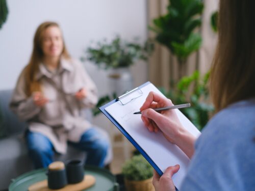 A therapist is sitting on a couch with a clipboard in front of her.