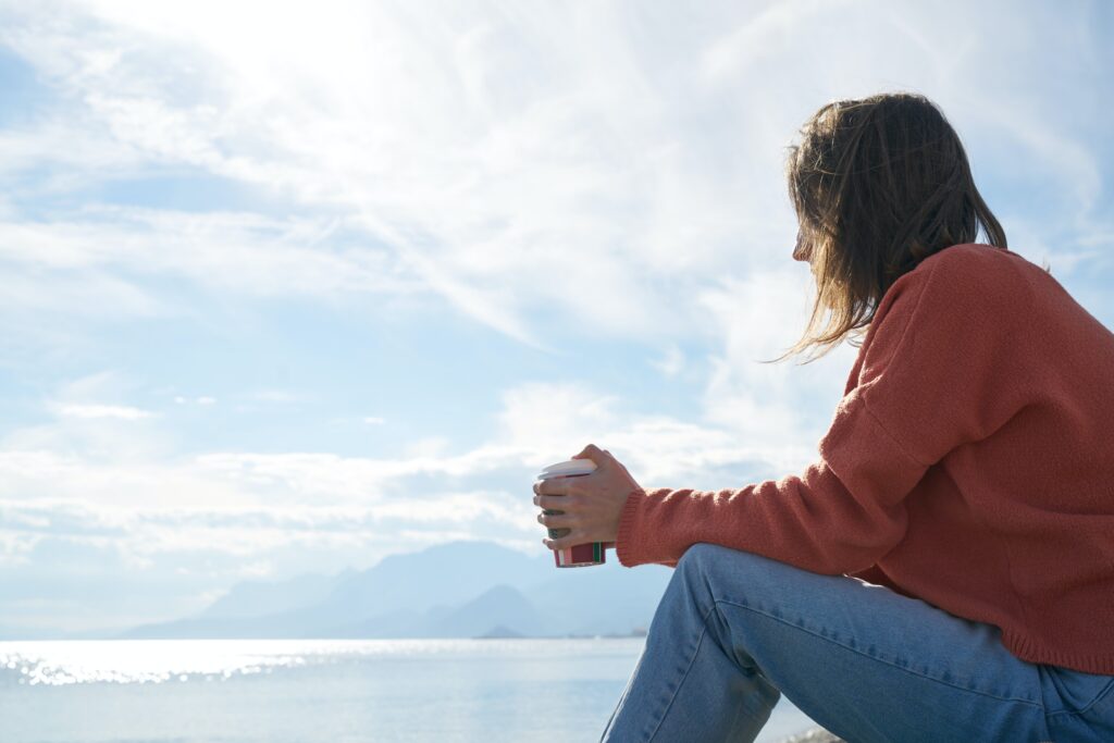 A woman, with an addict's brain wired to seek rewards, sitting on a rock with a cup of coffee.