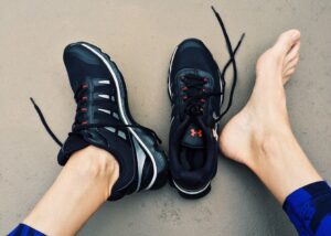 A person's feet in running shoes with arch support on a concrete floor, emphasizing the signs of need.