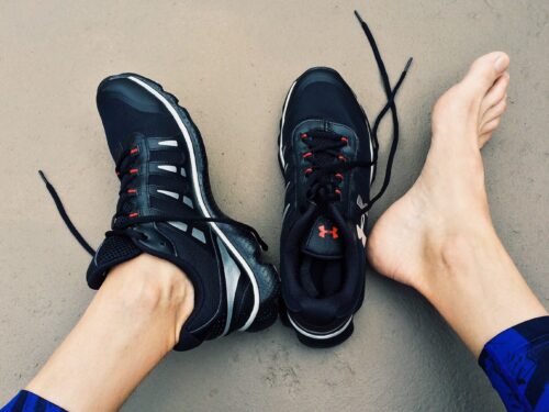 A person's feet in running shoes with arch support on a concrete floor, emphasizing the signs of need.