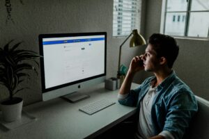 A man sitting in front of a computer looking at facebook.