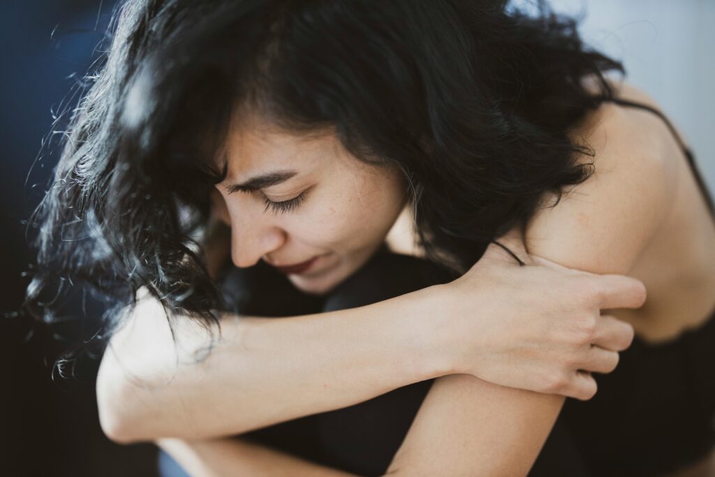 A young woman is hugging her arms in front of her face, possibly due to chronic pain.