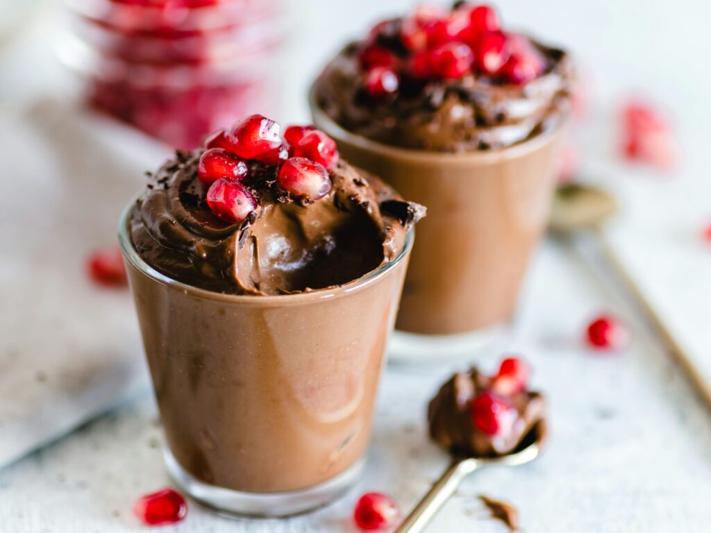 A romantic Valentine's Day recipe featuring two cups of indulgent chocolate mousse adorned with fresh pomegranate on top.