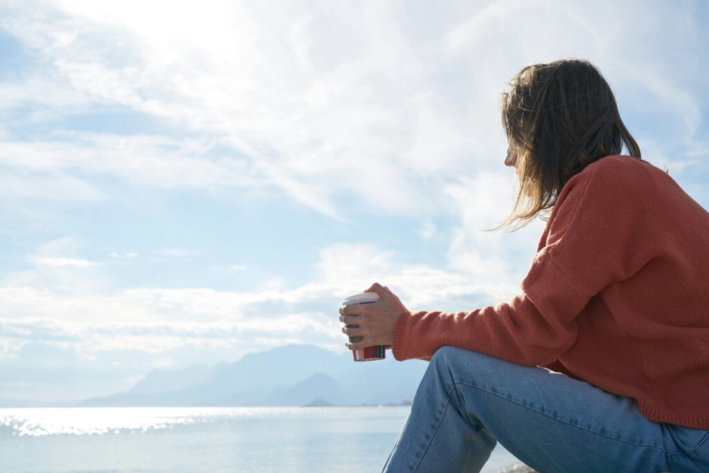 A woman with bipolar disorder sitting on a rock with a cup of coffee.