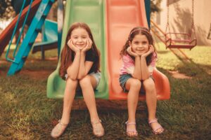 Two girls enjoying a colorful slide in a playground filled with climbing frames for kids.