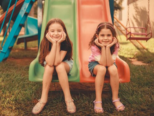 Two girls enjoying a colorful slide in a playground filled with climbing frames for kids.