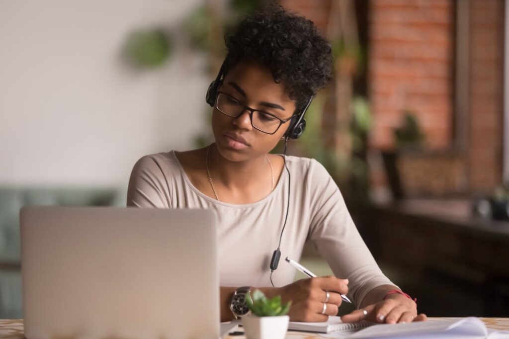 A woman working on a laptop is listening to music with headphones.