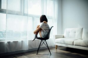 A woman sitting on a chair by a window, contemplating life.