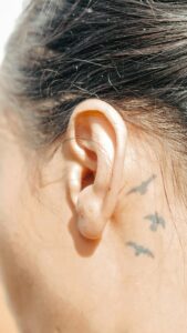 Close-up of a person's ear with a small tattoo of birds behind it, symbolizing their journey to overcome the stigma associated with hearing loss.