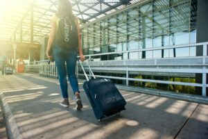 A person pulling a suitcase outside an airport hotel terminal.