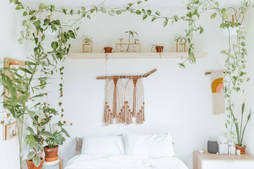 A serene Boho dorm bedroom interior with white bedding, houseplants, and hanging macramé decorations.