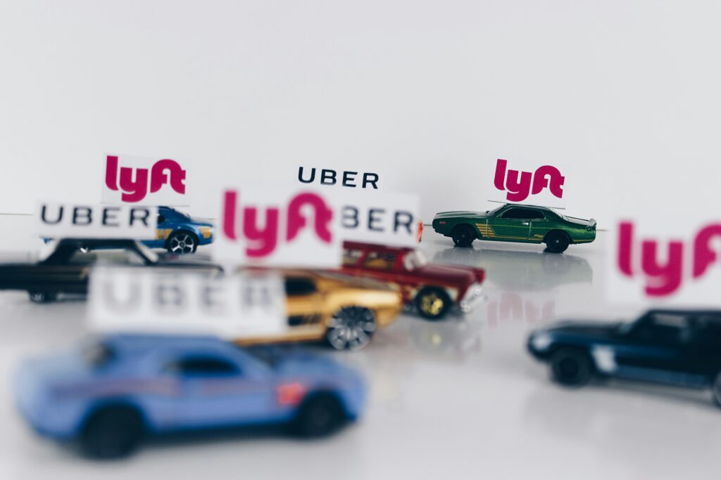 Toy cars positioned in front of Uber and Lyft logos, depicting ridesharing services.