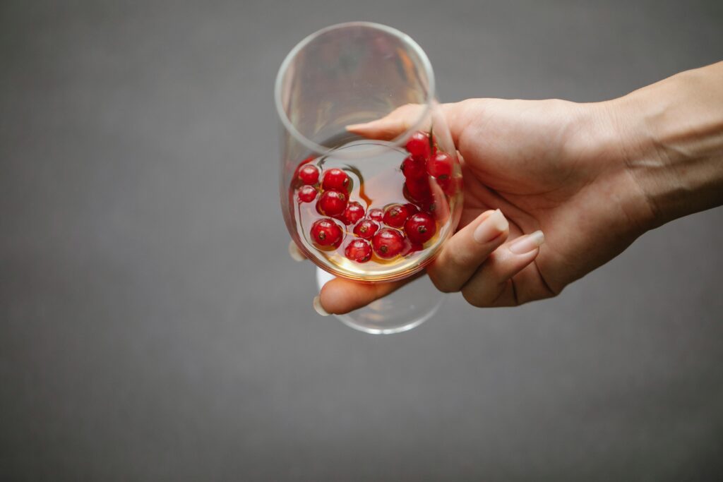 A hand holding a glass with red currant alcohol.