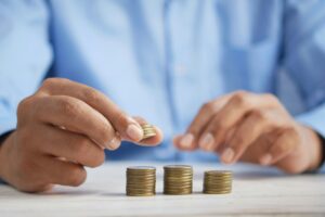 Person stacking coins in increasing columns on a table to address financial emergencies.