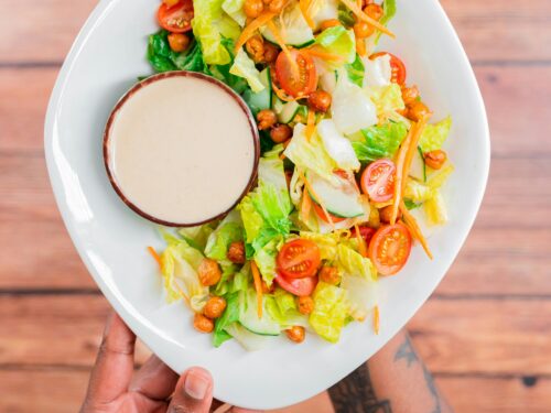 A person holding a plate of salad with a side of simple blender salad dressing.