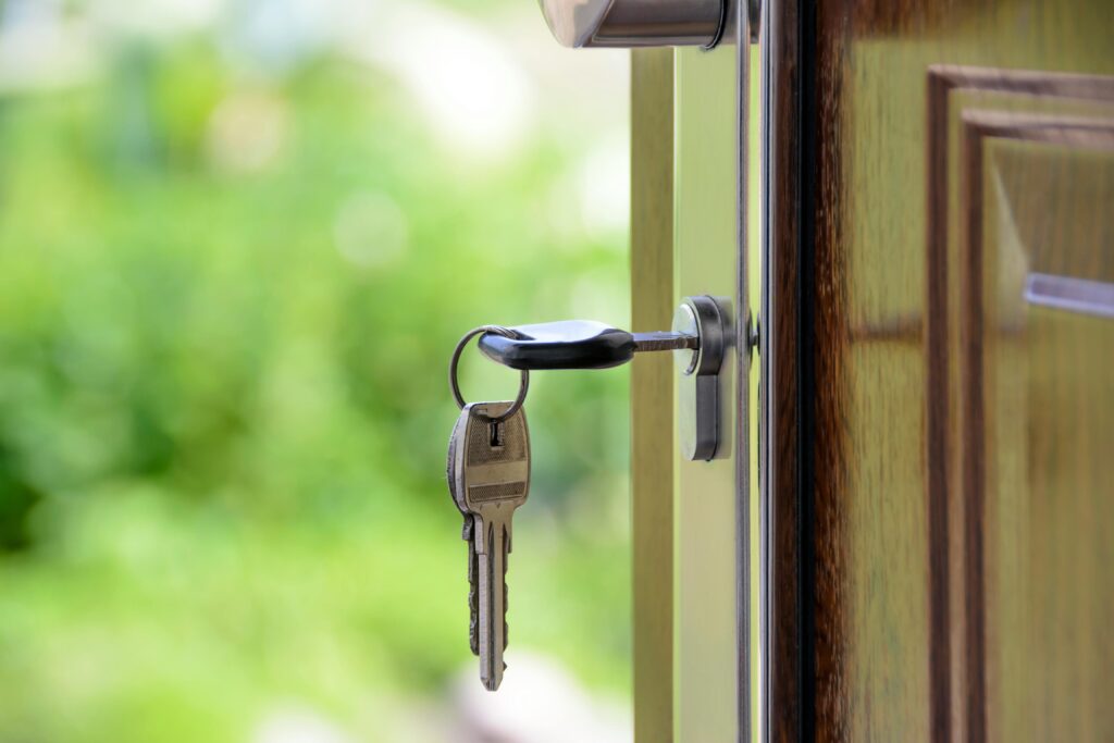 Keys hanging from an open door lock with a blurry green background, representing the first steps in a comprehensive guide for college students venturing into first-time renting.