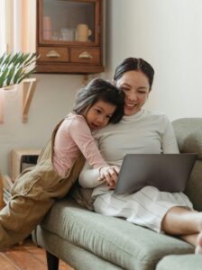 A young girl embraces a mompreneur from behind as they both look at a laptop screen together, navigating dual roles.